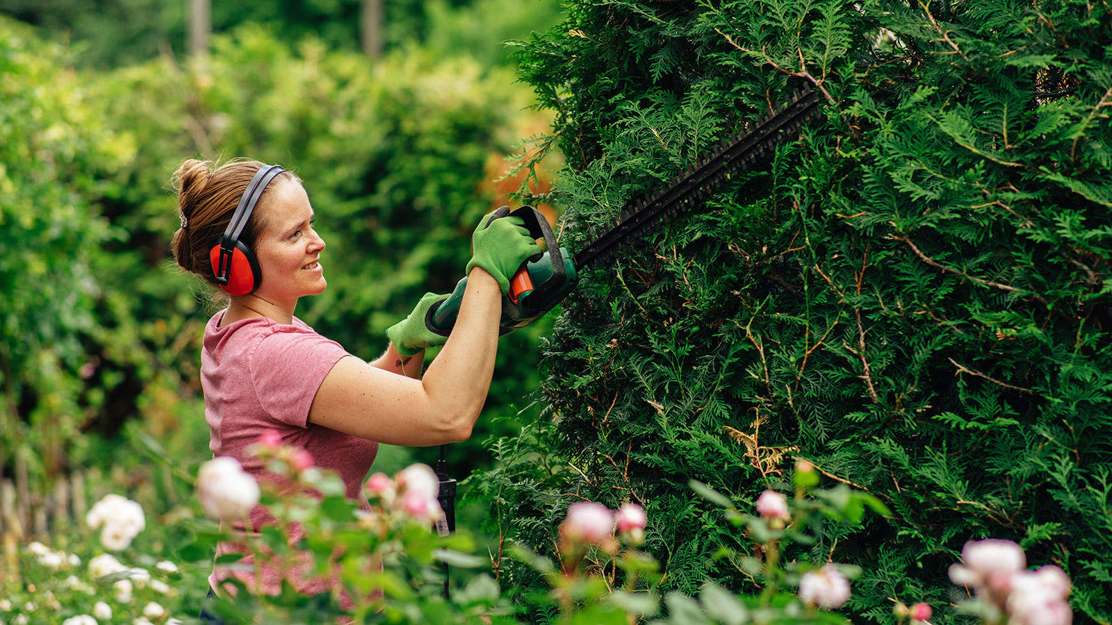 Kvinna arbetar med beskärning i villaträdgård som del av professionell trädgårdstjänst.